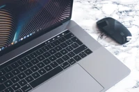 An Apple MacBook Pro and black Magic Mouse on a marble countertop.